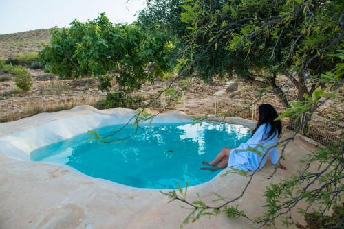 a woman sitting in a chair next to a small pool at Carmey Avdat Farm in Midreshet Ben Gurion