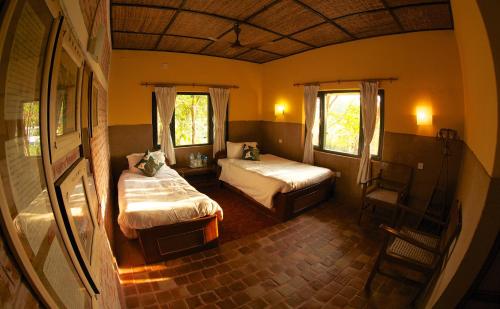 1 dormitorio con 2 camas, 1 silla y 2 ventanas en Maruni Sanctuary Lodge by KGH Group, en Sauraha