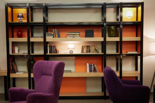two purple chairs in front of a book shelf at Vestil Hotel in Piotrków Trybunalski