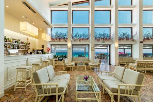 a lobby with chairs and a bar with the ocean in the background at Hotel Dei Pini in Alghero