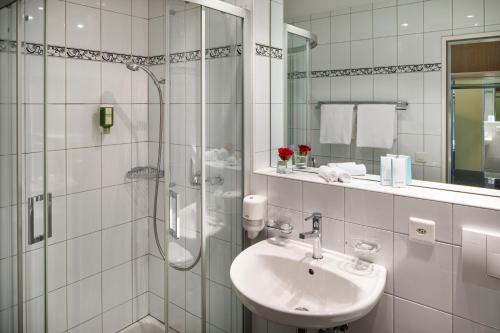 La salle de bains blanche est pourvue d'un lavabo et d'une douche. dans l'établissement Beinwil Swiss Quality Seehotel, à Beinwil