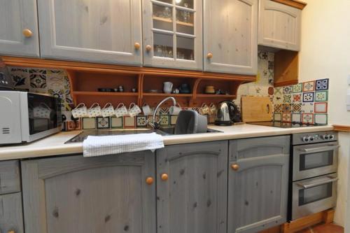 a kitchen with white cabinets and a sink and a microwave at Shipwrights Cottage in Salcombe