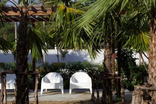 two white chairs and palm trees in a yard at Chez Bure - Bure Homestay in Kanchanaburi