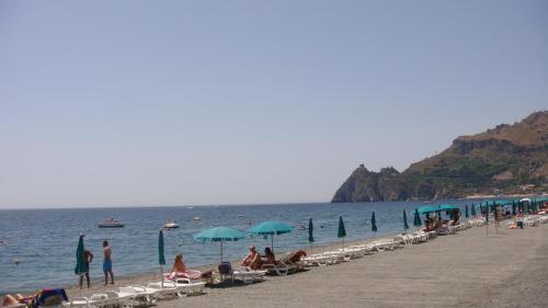 a group of people sitting on a beach with umbrellas at Hotel Kennedy in SantʼAlessio Siculo