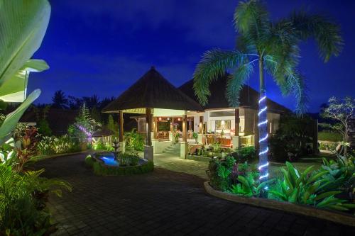 a villa with a palm tree and a house with lights at Anusara Luxury Villas in Ubud