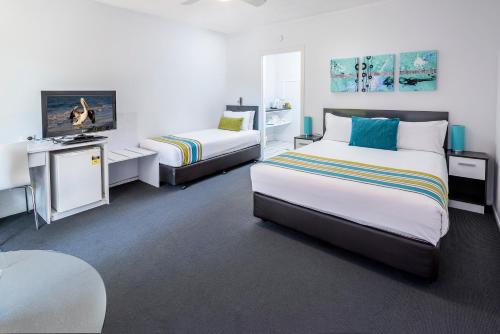 a hotel room with two beds and a television at The Beach Motel Hervey Bay in Hervey Bay