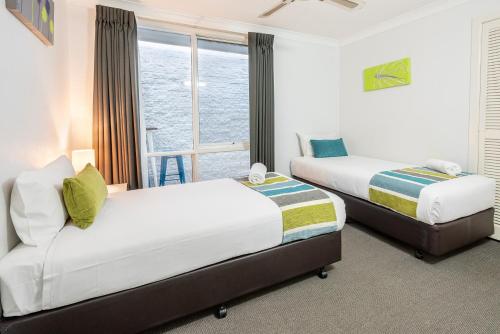 two beds in a hotel room with a window at The Beach Motel Hervey Bay in Hervey Bay