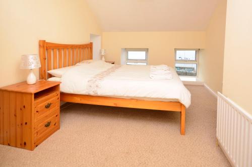 a bedroom with a bed and a nightstand and two windows at Cottage 236 Roundstone in Roundstone