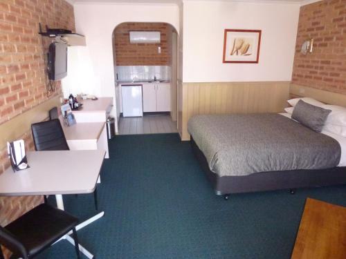 a room with a bed and a desk and a kitchen at Colonial Motor Inn Bairnsdale Golden Chain Property in Bairnsdale