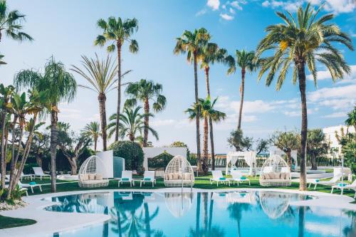 uma piscina com palmeiras e cadeiras brancas em Iberostar Selection Marbella Coral Beach em Marbella