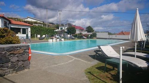 a swimming pool with two chairs and an umbrella at Hotel Jardim Atlantico in Calheta