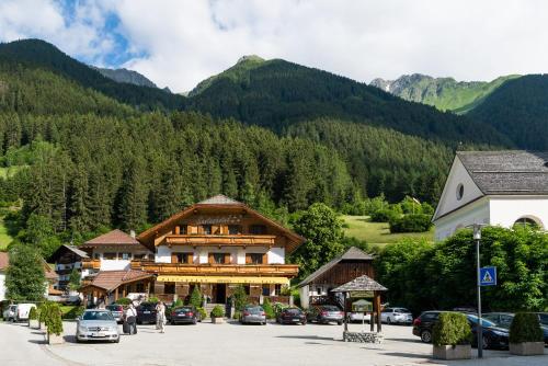 a building with cars parked in a parking lot with mountains at Santeshotel in Anterselva di Mezzo