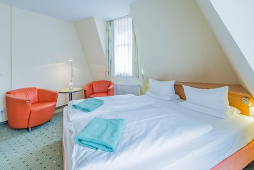 a bedroom with a white bed and two orange chairs at Am Weststrand Aparthotel Kühlungsborn in Kühlungsborn