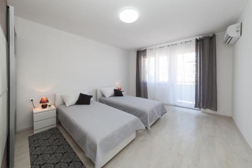 a white bedroom with two beds and a window at Apartman Bordura in Zadar