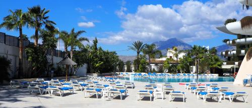 a group of chairs and a pool with mountains in the background at Hotel Deloix 4* Sup in Benidorm