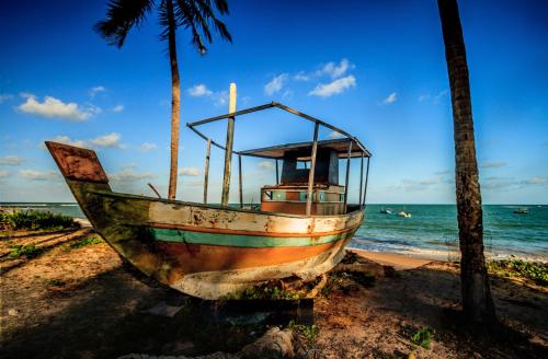 a boat sitting on the beach next to the ocean at Apartamentos Breezes com verde, sossego e preço justo - ideal para famílias e amigos em Imbassaí in Imbassai