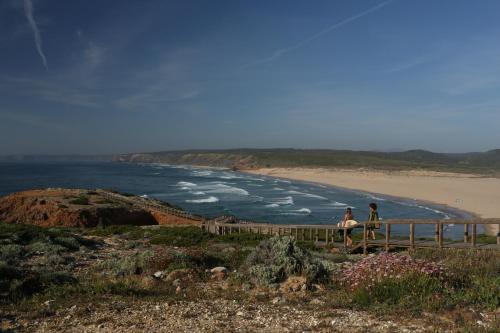 two people sitting on a fence near a beach at Memmo Baleeira - Design Hotels in Sagres