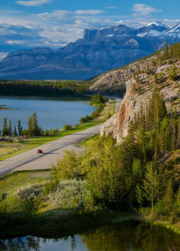 a road with a lake and mountains in the background at Overlander Mountain Lodge in Jasper
