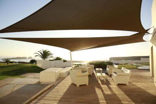 a patio with white chairs and a large umbrella at Memmo Baleeira - Design Hotels in Sagres