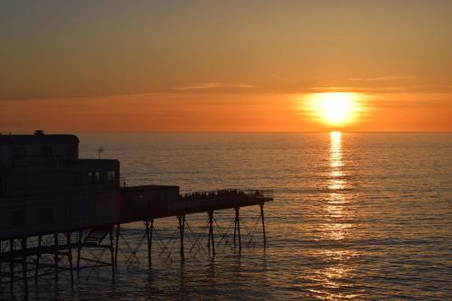 a pier with the sun setting over the ocean at Awel Mor Holiday Apartment in Aberystwyth