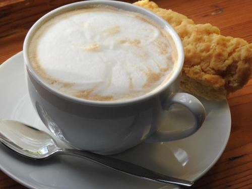 a cup of coffee on a plate with a piece of food at The Featherbed - Oudtshoorn in Oudtshoorn