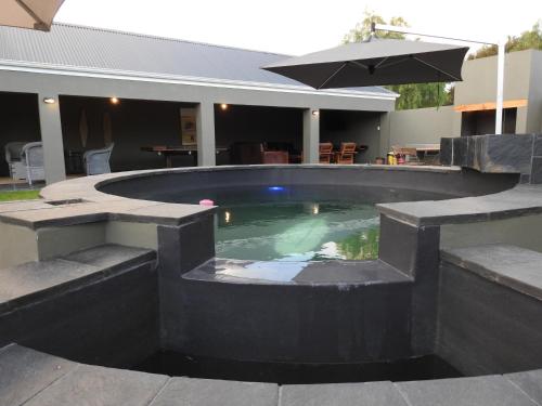 a swimming pool with benches and an umbrella at The Featherbed - Oudtshoorn in Oudtshoorn