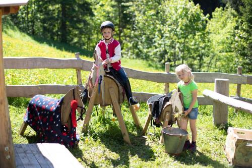 two children playing on a wooden toy horse at Vital Chalets in Schröcken