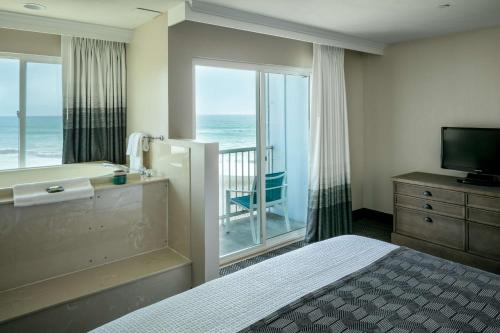 a bedroom with a tub and a balcony with the ocean at Beachfront Inn in Brookings