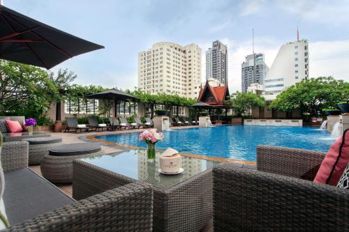 een zwembad met stoelen en een tafel met bloemen bij The Sukosol Hotel in Bangkok