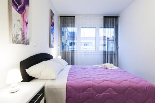sypialnia z fioletowym łóżkiem i oknem w obiekcie Apartments Kalelarga w mieście Zadar