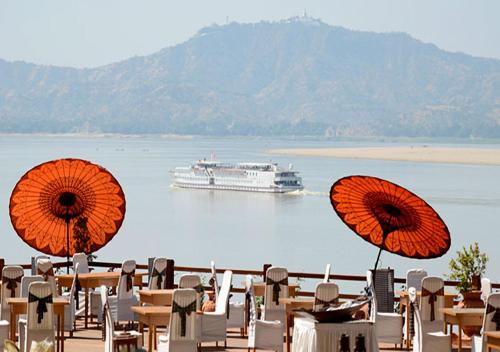 a cruise ship on the water with tables and umbrellas at KMA Bagan Hotel River View in Bagan