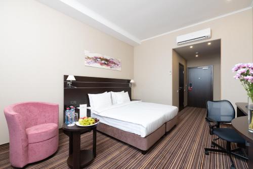 um quarto de hotel com uma cama e uma cadeira rosa em Armat Hotel em Irkutsk