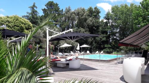 a pool with people sitting under umbrellas next to a pool at Mercure Bordeaux Lac in Bordeaux