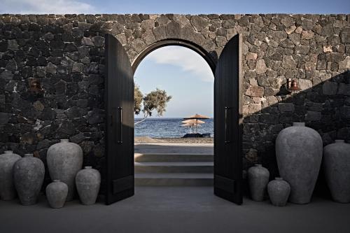 una porta aperta su un muro di pietra con vista sull'oceano di Istoria, a Member of Design Hotels a Perivolos