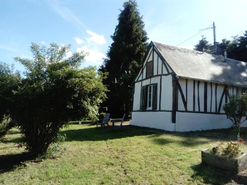 une maison blanche et noire avec une personne assise dans la cour dans l'établissement La petite maison normande, à Ticheville