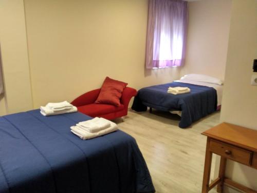 Habitación con 2 camas y silla roja. en Hostal Orly, en Camponaraya