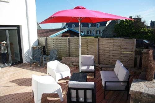 een patio met witte stoelen en een rode parasol bij Maison de Poul Briel in Saint-Guénolé