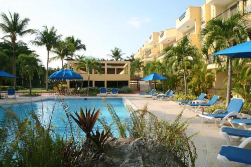 una piscina con sillas azules y sombrillas en un complejo en Garden Condos, en Sosúa