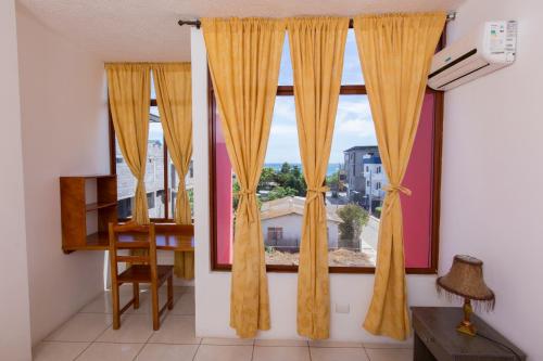a window with yellow curtains in a room with a desk at Hostal Tongo Reef in Puerto Baquerizo Moreno
