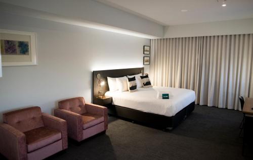 ジェラルトンにあるThe Gerald Apartment Hotelのベッド1台と椅子2脚が備わるホテルルームです。