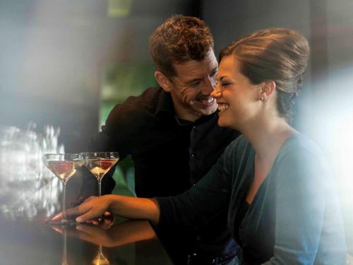 a man and a woman looking at a wine glass at Novotel Athens in Athens