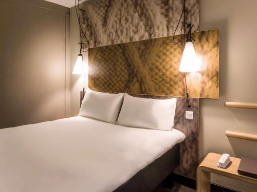 a bedroom with a bed with white sheets and lights at ibis Amsterdam City West in Amsterdam