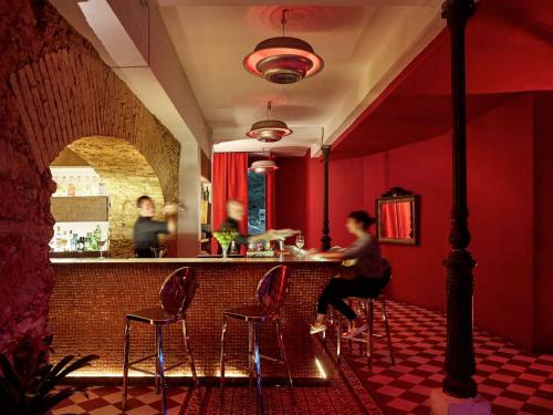 a woman sitting at a bar in a red room at Santa Teresa Hotel Rio de Janeiro - MGallery Collection in Rio de Janeiro