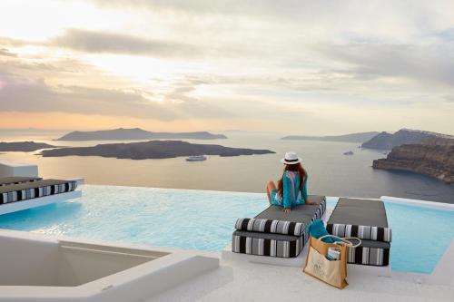 a woman sitting on the edge of a infinity pool overlooking the ocean at Alti Santorini Suites - Caldera View in Megalochori