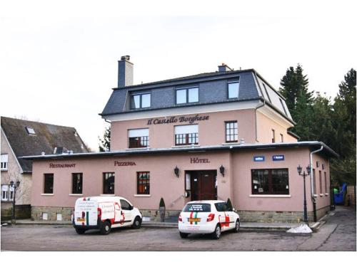 twee auto's geparkeerd voor een roze gebouw bij Hotel il Castello Borghese in Senningerberg