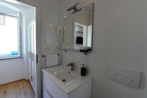 a white bathroom with a sink and a mirror at Apartments and Rooms Oliva in Cres