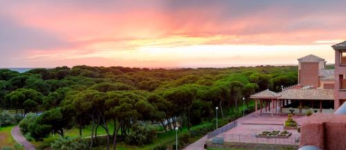 a view of a building and trees with a sunset at Barceló Punta Umbría Beach Resort in Punta Umbría