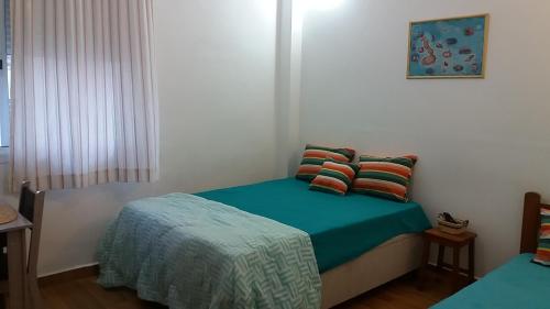 a bedroom with a bed with a green blanket and pillows at Kitnet Guarujá - Pitangueiras - sem garagem in Guarujá