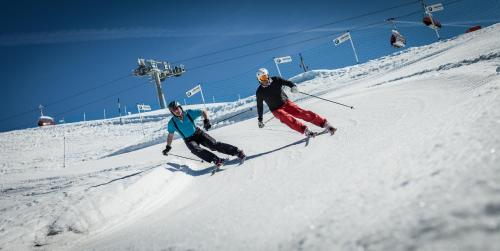two people are skiing down a snow covered slope at Aktivhotel Tuxerhof in Zell am Ziller