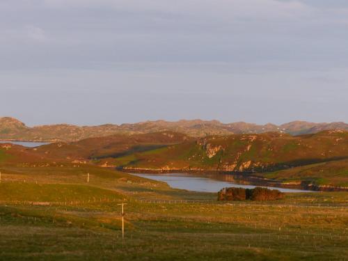 a lake in the middle of a field with hills at Glenhouse in Leurbost